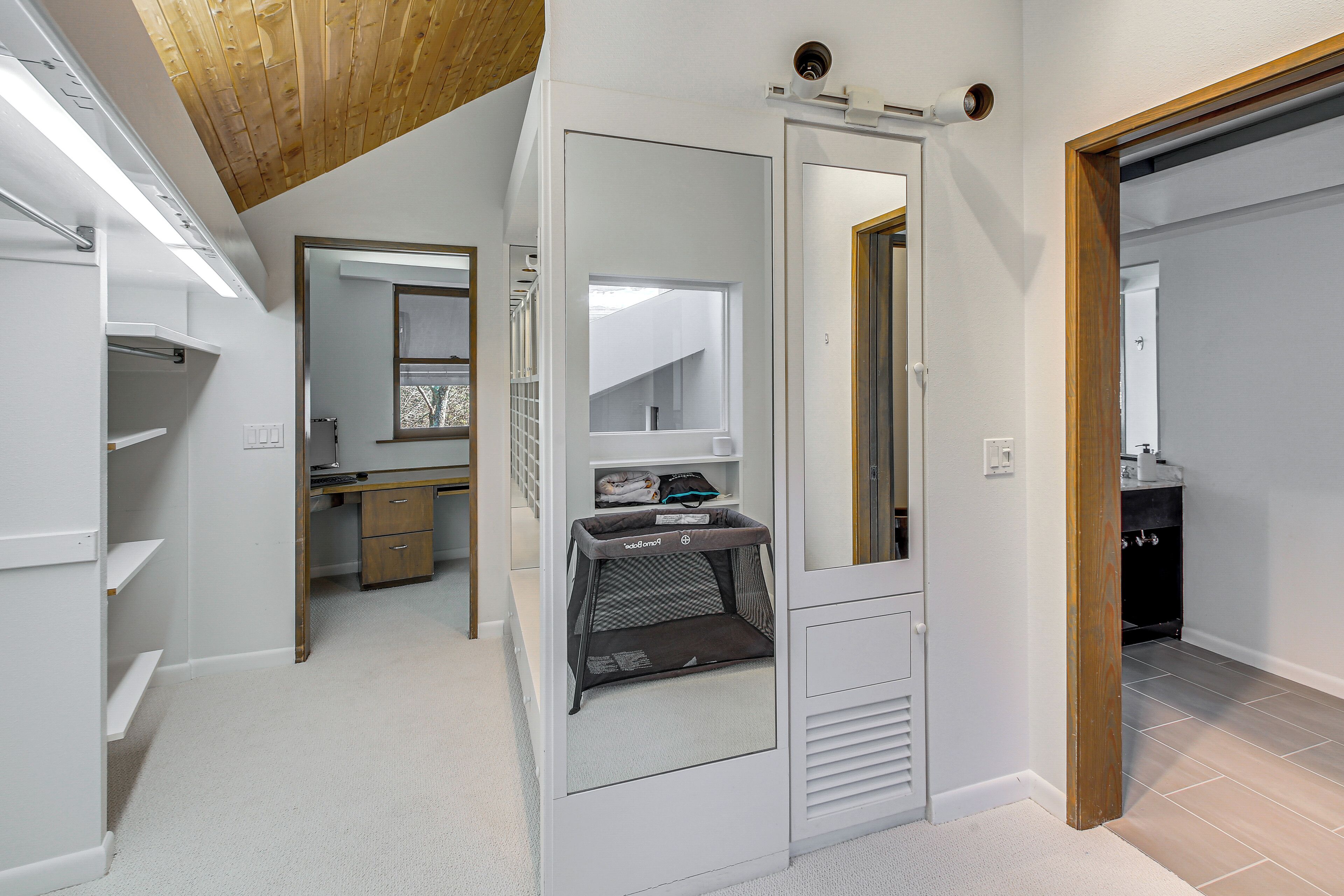 A modern room with a wooden ceiling, a large mirror, a baby playpen, and a view of a balcony.