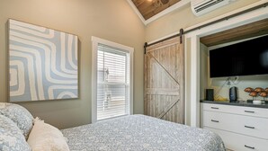 Une chambre à coucher avec un lit, une grande fenêtre avec des stores, une armoire en bois et un téléviseur à écran plat posé sur une commode.