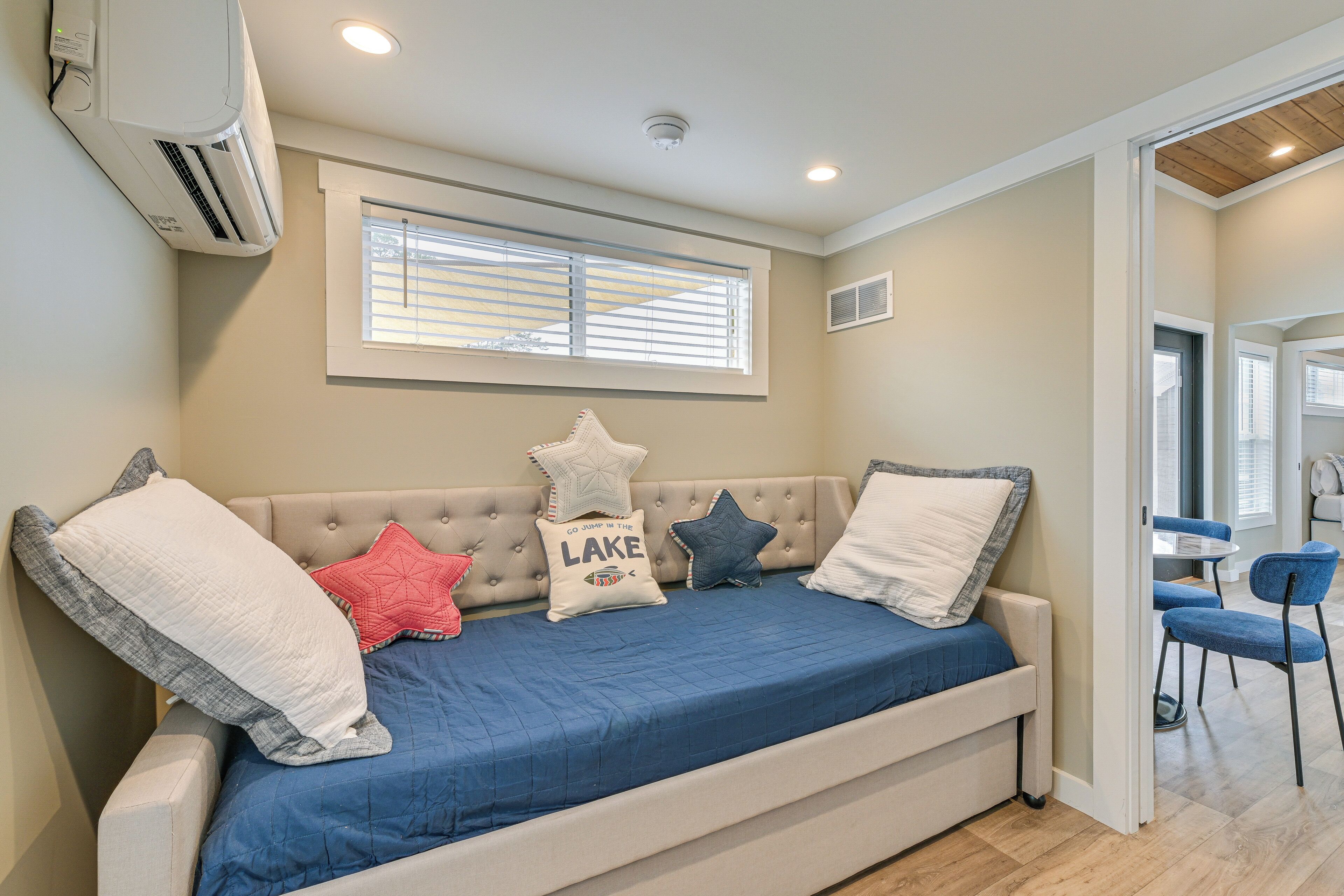 A cozy room with a beige sofa, a blue bedspread, and a window with blinds.