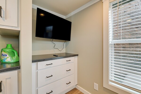 A kitchen with a flat-screen TV mounted above a white cabinet with drawers, a green bottle of Purex dish soap on the counter, and a window with blinds. - < 1 Mi to Marina: Pet-friendly Lake Norman Home! (Sherrills Ford)