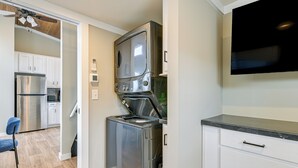 Une cuisine compacte équipée d’un four encastré, d’un réfrigérateur en acier inoxydable et d’un téléviseur à écran plat fixé au mur.