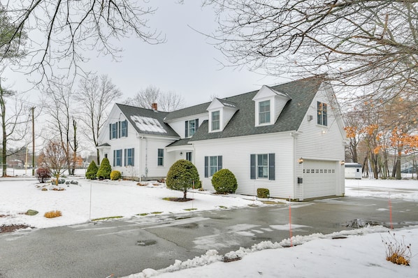 A two-story house with a garage, surrounded by snow-covered ground and leafless trees.