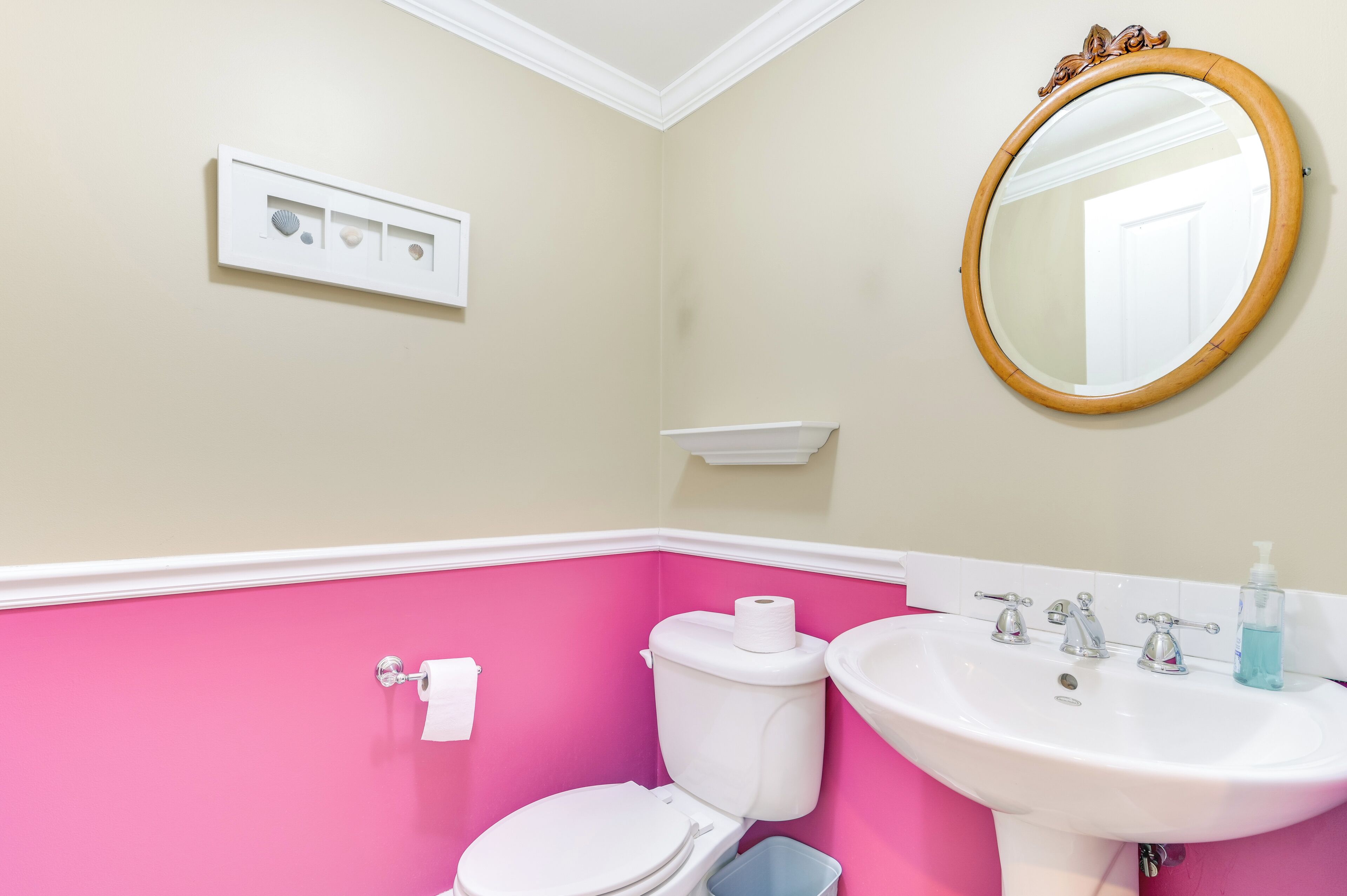 A bathroom with a toilet, sink, mirror, and a wall-mounted shelf.