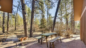 A patio with picnic tables and benches, surrounded by tall trees.