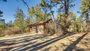 A wooden cabin with a garage, surrounded by tall pine trees and a clear sky.