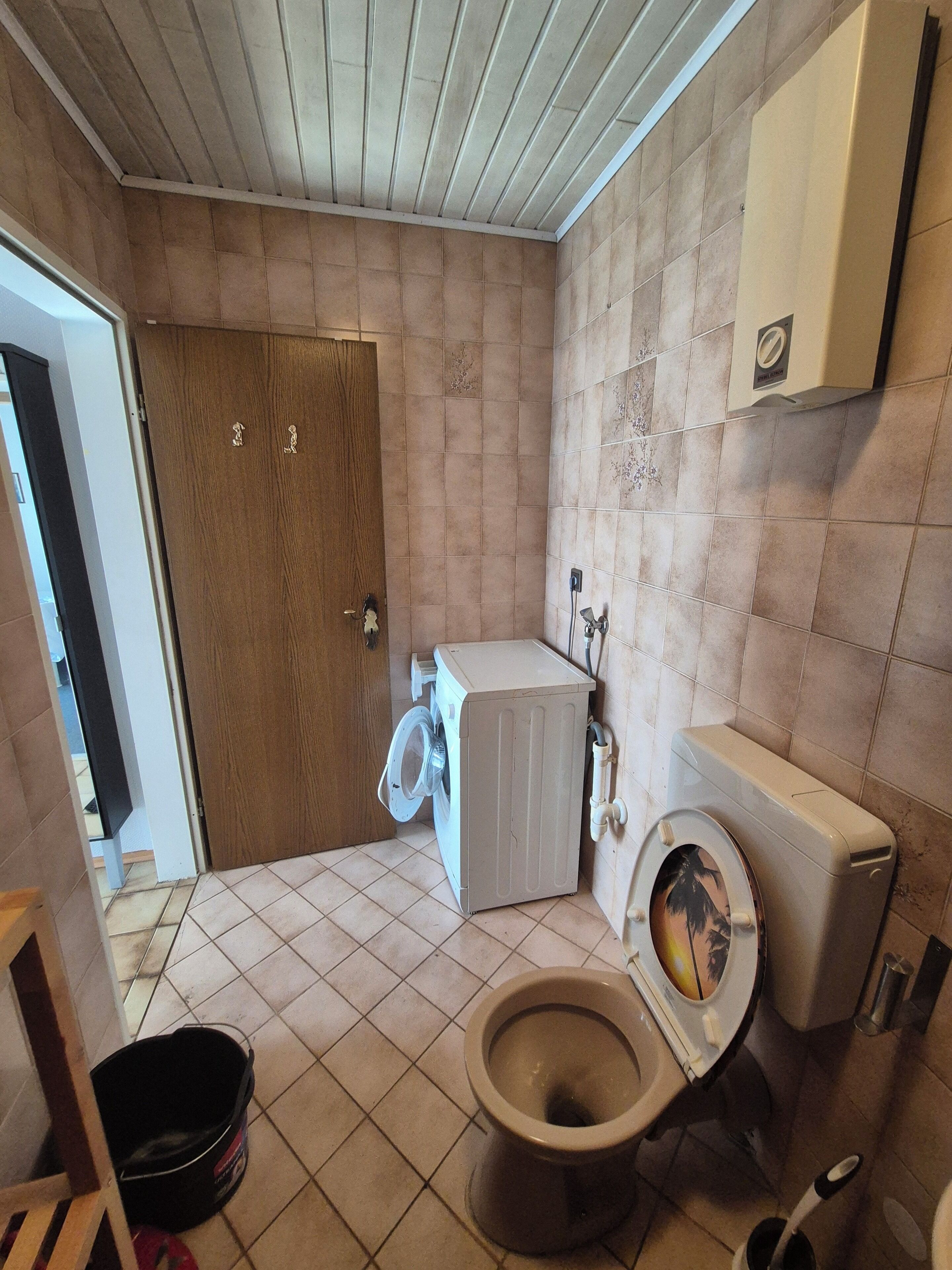 Une petite salle de bain comprenant des toilettes, un lave-linge et une porte en bois.
