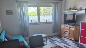 A room with a wooden ceiling, a television on a cabinet, a dining table with chairs, a sofa, and a window with curtains. - Vacation apartment Puth (Koblenz)