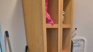 A wooden cabinet with multiple shelves, a mop leaning against it, and a plastic container with cleaning supplies. - Vacation apartment Puth (Koblenz)