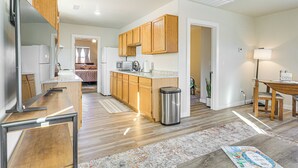 A modern kitchen with wooden cabinets, a stainless steel trash can, and a dining area with a table and chairs. - 3 Mi to Elephant Butte Lake: Cozy Retreat! (Truth or Consequences)