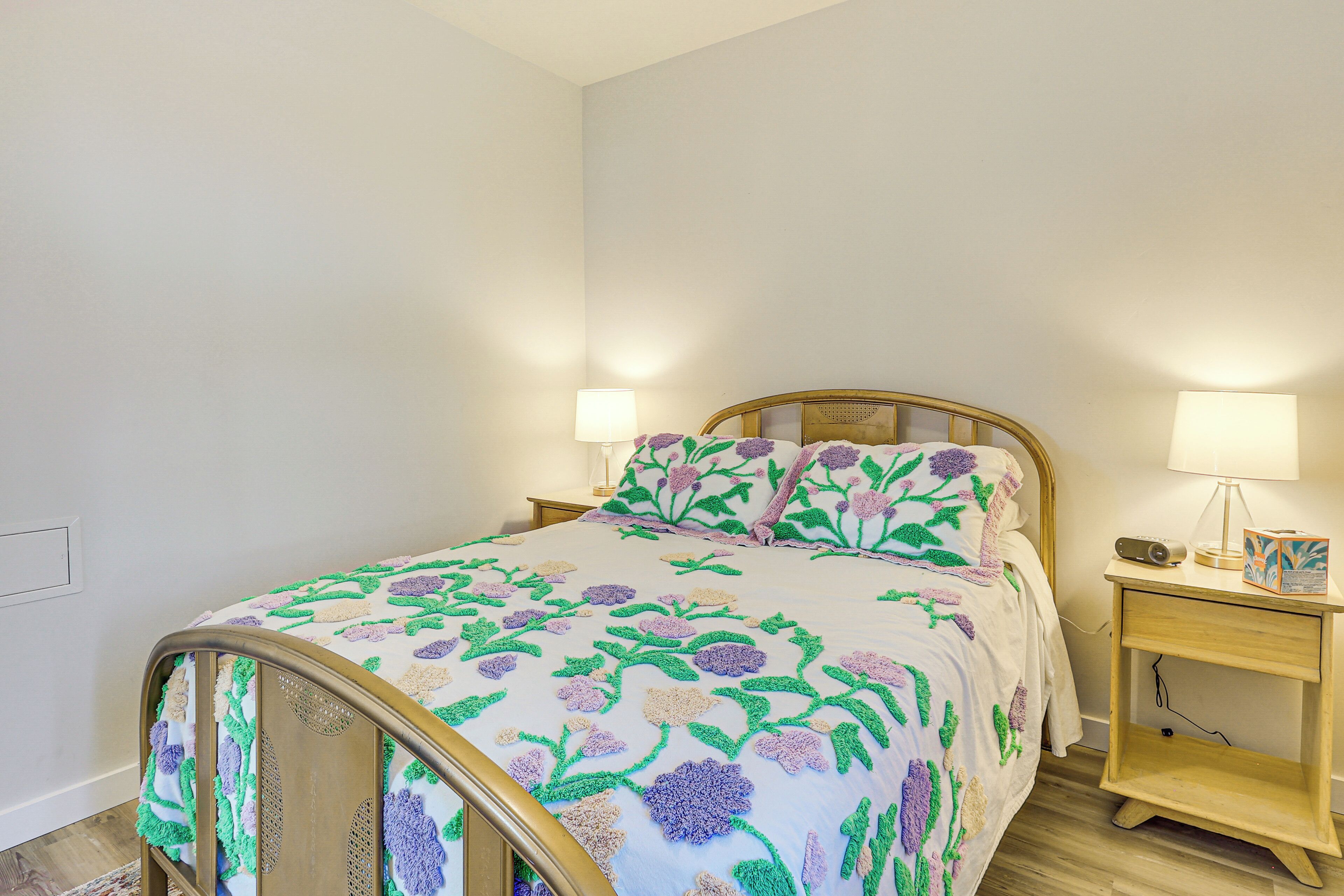 Een slaapkamer met een houten bed, bloemenbedrukking, twee nachtkastjes met lampen en een nachtkastje met een radio.