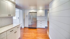 Una cocina con armarios blancos, un refrigerador de acero inoxidable y piso de madera.