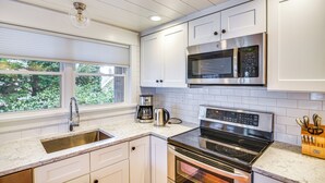 A modern kitchen with white cabinets, stainless steel appliances, and a window with a view of greenery.