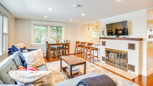 A spacious living room with a fireplace, a television mounted above it, and a dining area with wooden chairs and a table.