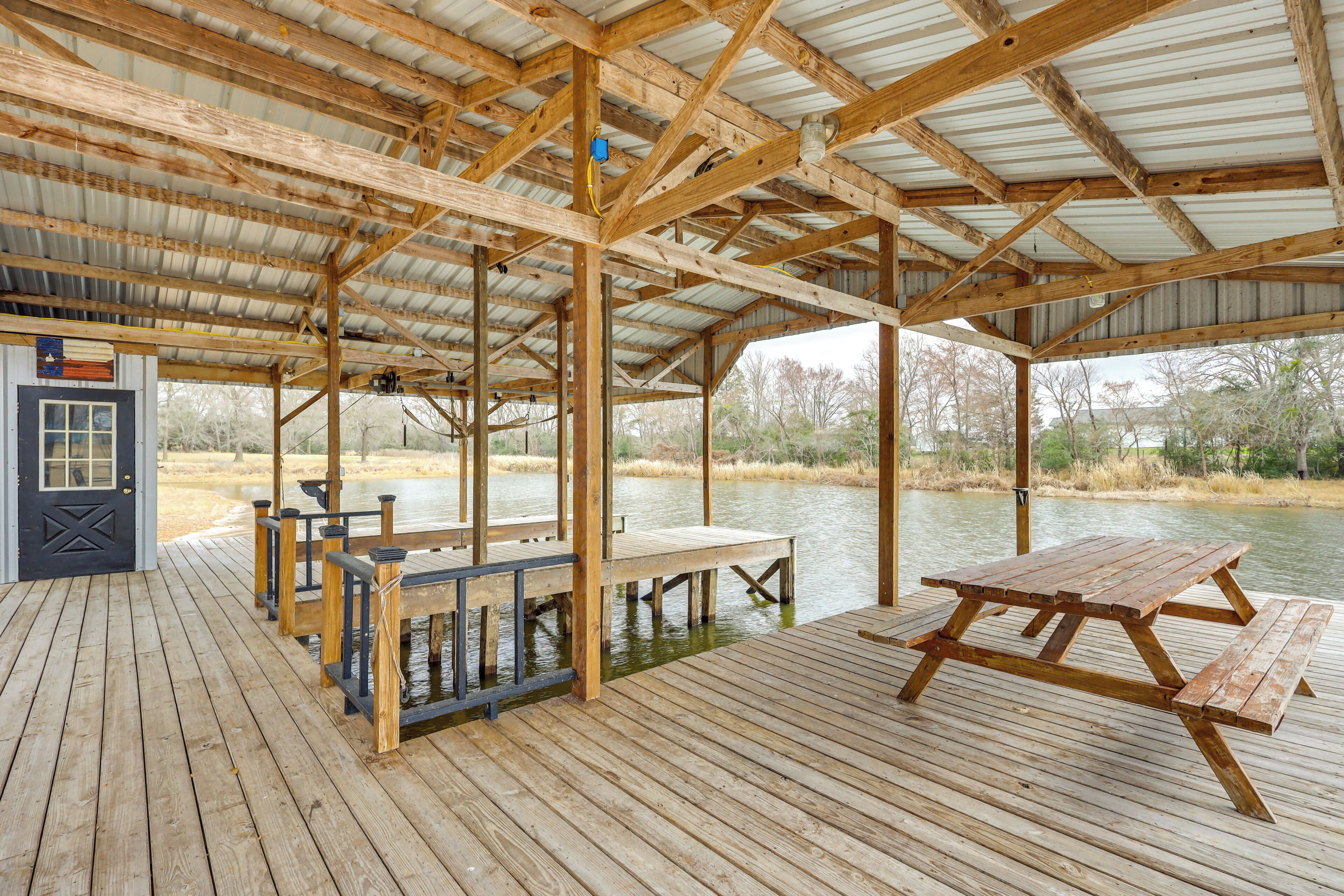 A covered wooden deck with a picnic table and benches, overlooking a body of water.