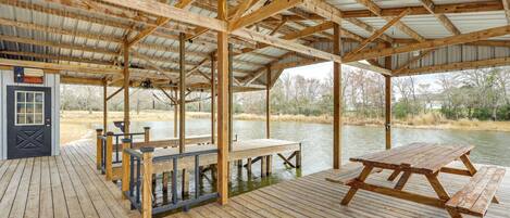 A covered wooden deck with a picnic table and benches, overlooking a body of water.