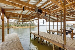 Eine Holzterrasse über dem Wasser mit Bänken und Tischen, gestützt von Holzbalken und einem Metalldach.
