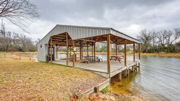 A covered outdoor pavilion with a wooden deck, tables, and benches by a lake.