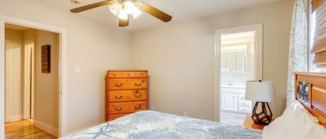 Un dormitorio con cama, cómoda de madera, ventilador de techo y mesita de noche con lámpara.