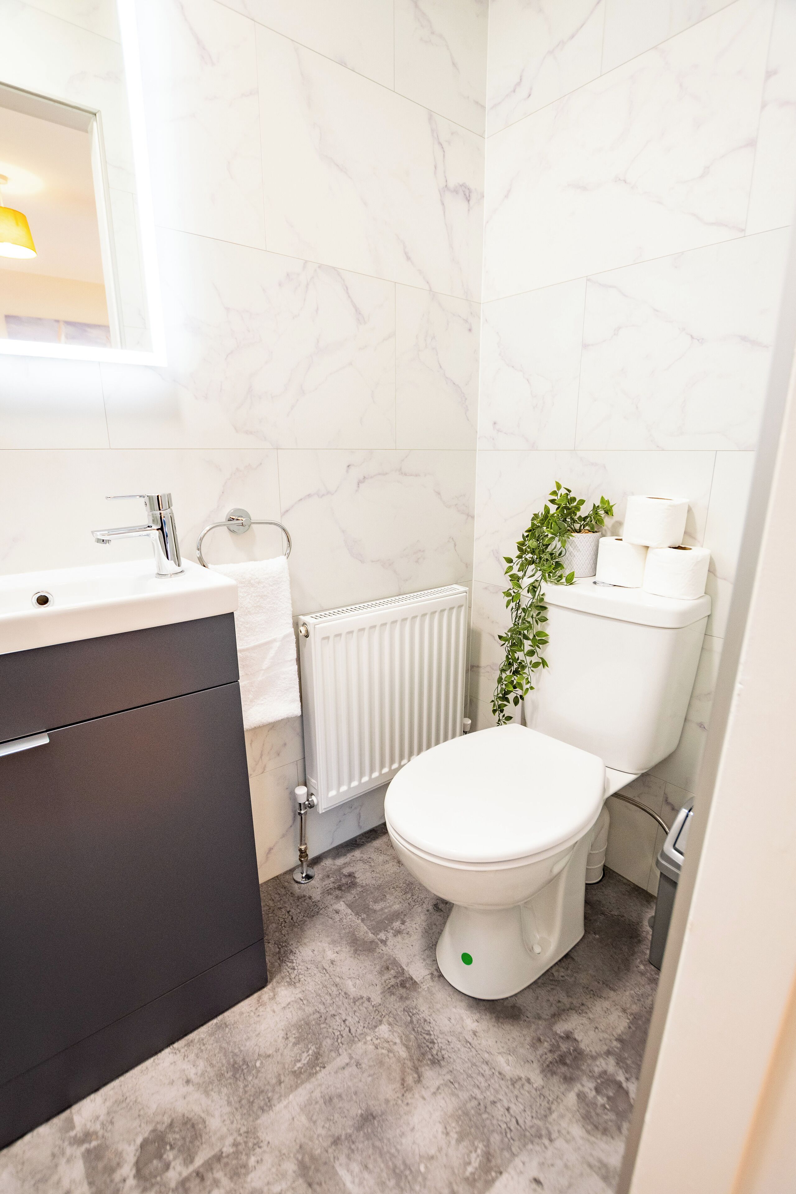 A modern bathroom with a white toilet, a sink with a mirror, and a radiator.