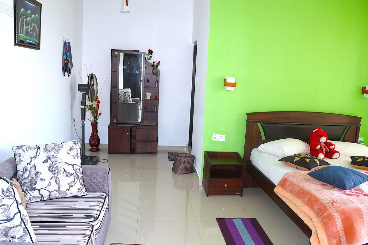 A hotel room with a bed, a sofa, a dresser, and a mirror.
