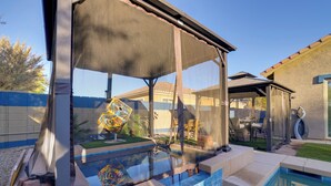 A swimming pool with a covered area, steps, and outdoor furniture. - Putting Green & Hot Tub: Goodyear Retreat! (Goodyear)