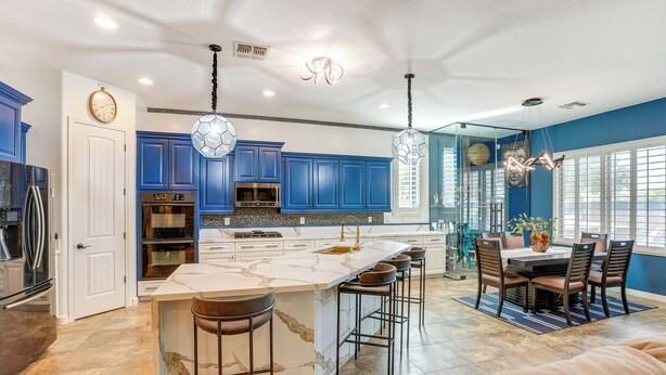 A modern kitchen with blue cabinets, a marble island, and bar stools. - Putting Green & Hot Tub: Goodyear Retreat! (Goodyear)