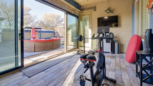 A home gym with exercise equipment, a television, and a sliding glass door leading to an outdoor patio. - Putting Green & Hot Tub: Goodyear Retreat! (Goodyear)