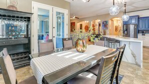 A modern kitchen with a central island, a dining area with a glass-top table, and a decorative vase with flowers. - Putting Green & Hot Tub: Goodyear Retreat! (Goodyear)