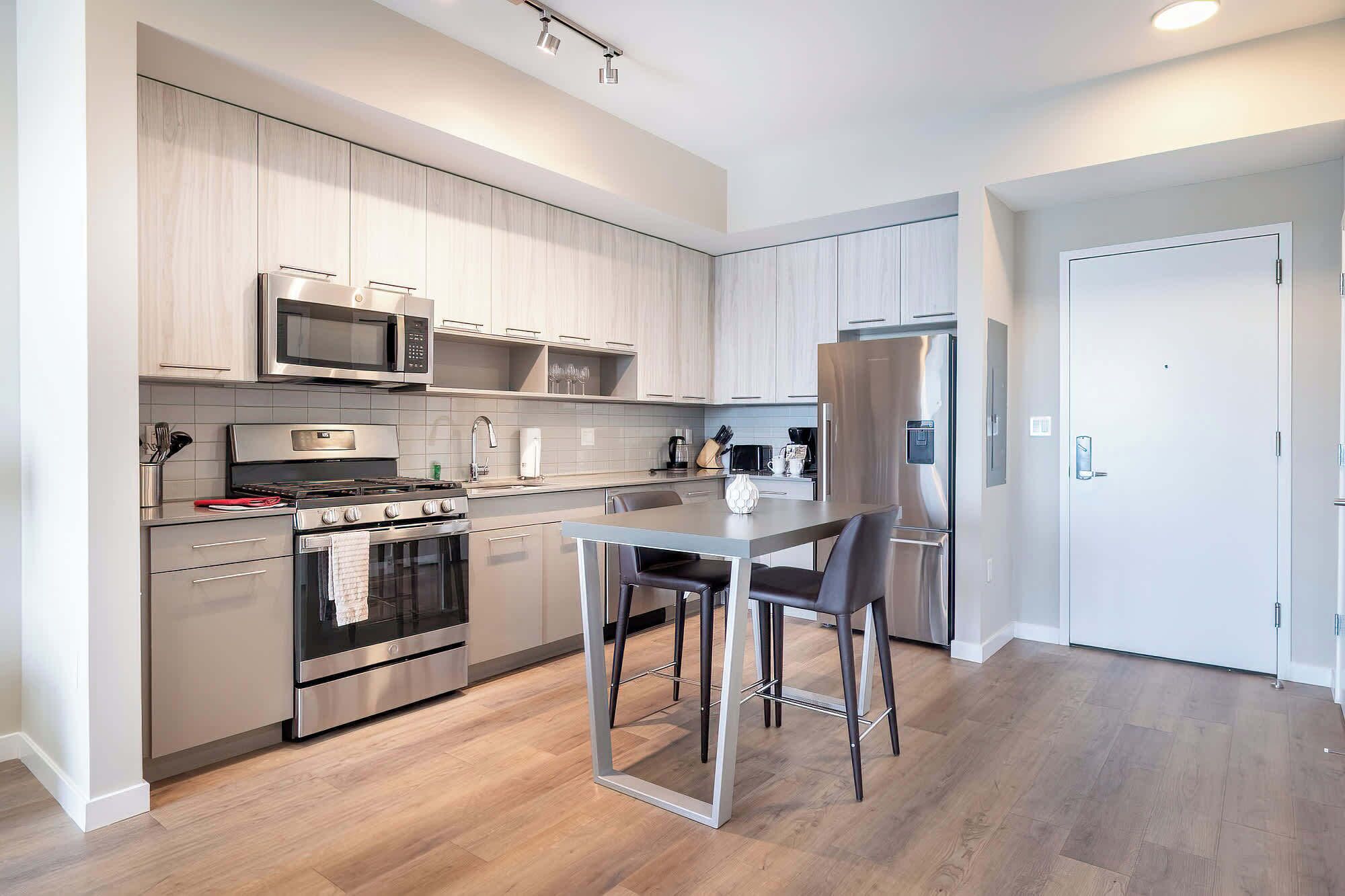 A modern kitchen with stainless steel appliances, a dining area with a table and chairs, and light wood flooring.