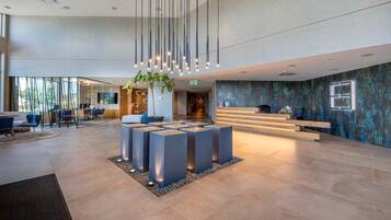 A modern lobby with a reception desk, seating area, and a large plant centerpiece.
