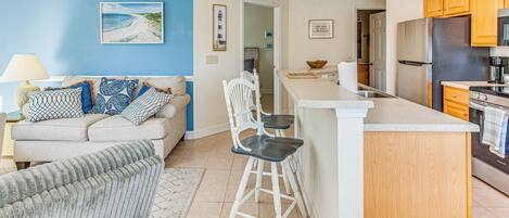 A modern kitchen with wooden cabinets, a stainless steel refrigerator, and a bar area with stools.