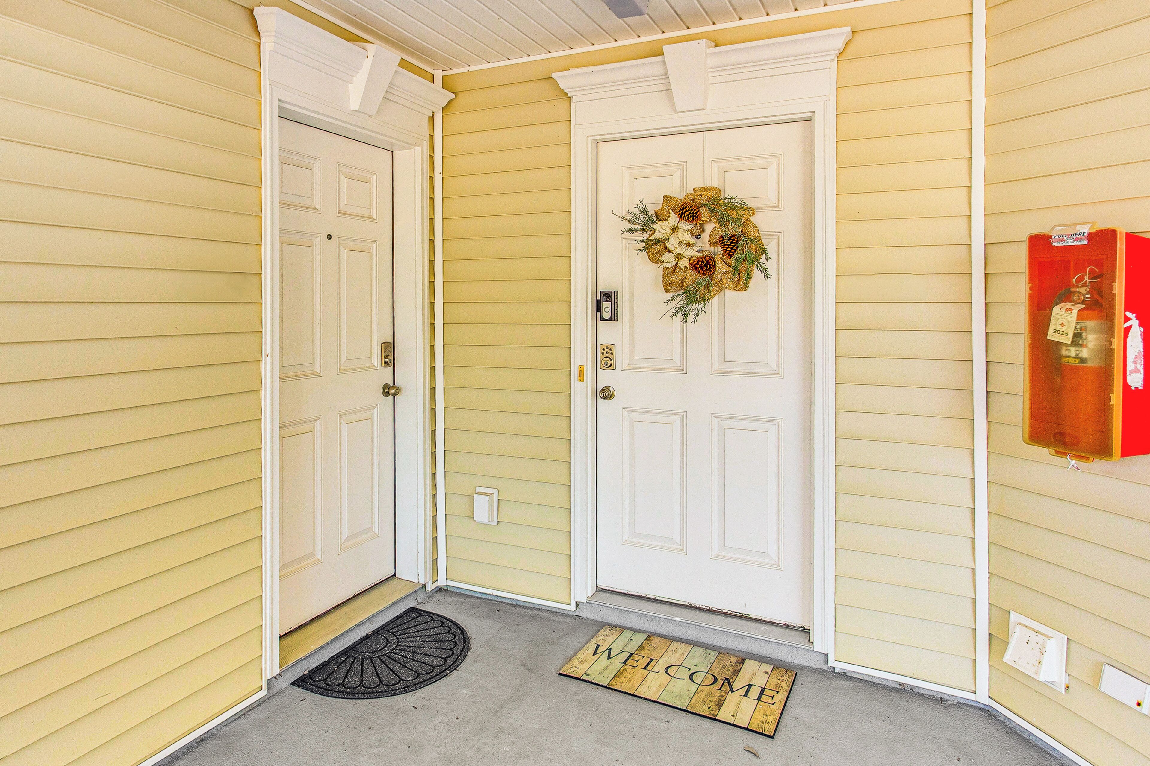 A yellow house with a white front door, a welcome mat, and a fire extinguisher on the wall.