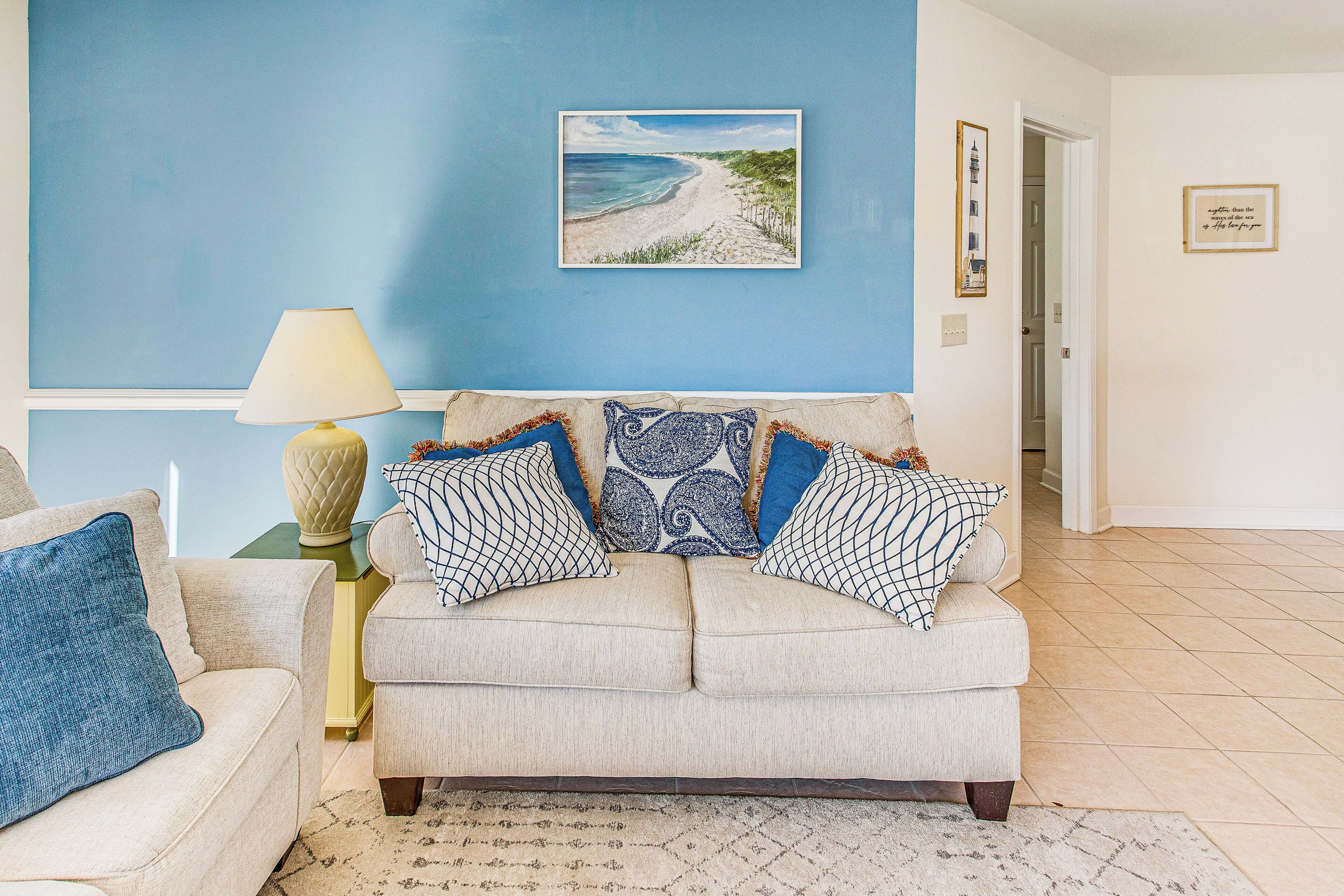 A living room with a beige sofa, a blue wall, and a framed beach painting.