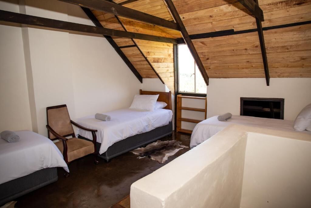 A room with two beds, a chair, a fireplace, and a sloped wooden ceiling.