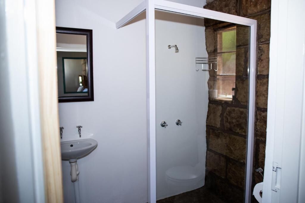 Un baño con lavamanos blanco, un espejo y una ducha con pared de piedra.