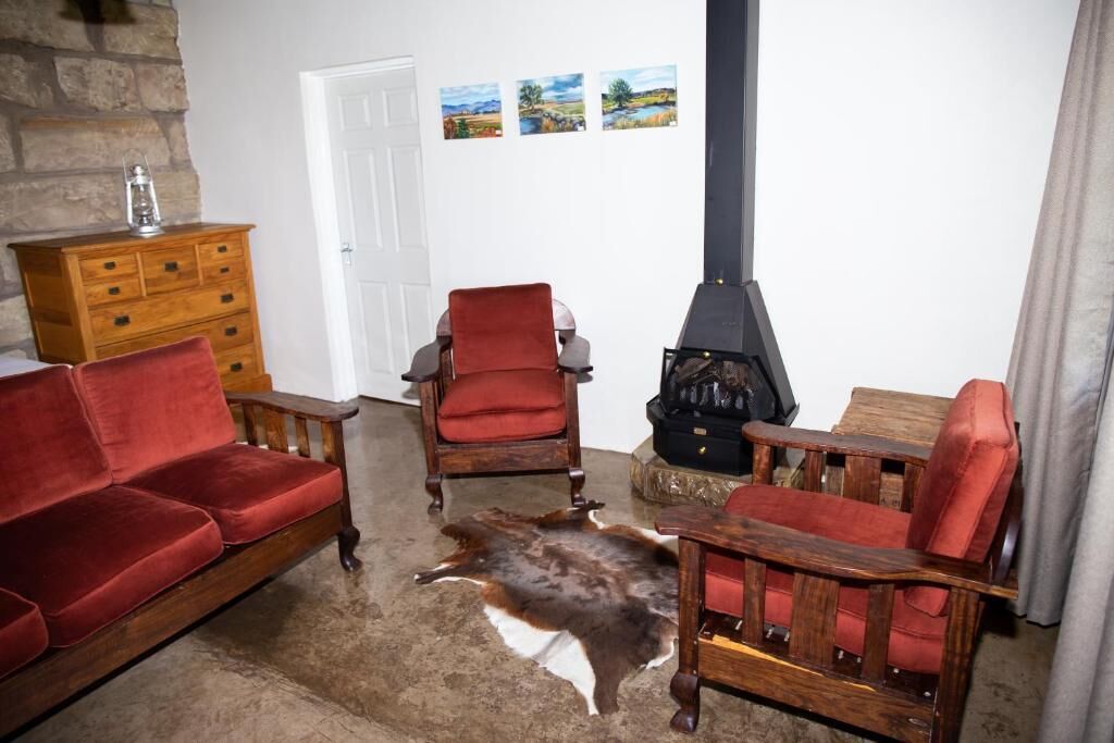 Un salon chaleureux avec un canapé rouge, une chaise en bois, un divan en cuir, une cheminée en pierre et une table en bois.