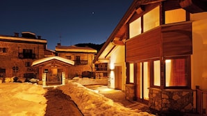 Un patio cubierto de nieve con un sendero de piedra que conduce a un edificio de madera con ventanas amplias y una entrada de piedra.