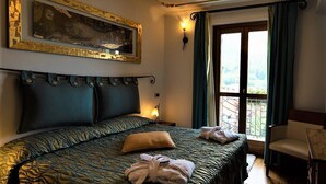 Un dormitorio con cama, una silla, un ventanal con cortinas, un cuadro en la pared y una lámpara de araña.