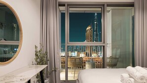 Une chambre d’hôtel avec un grand lit, un bureau et une vue sur les toits illuminés de la ville la nuit.