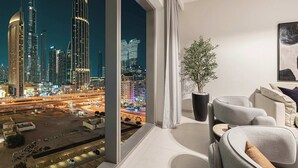 Un salon moderne doté d’une grande fenêtre donnant sur une vue nocturne de la ville, avec de hauts immeubles et une rue animée.