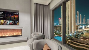 Un salon moderne avec une cheminée, des canapés gris et une grande fenêtre donnant sur une vue panoramique de la ville la nuit.