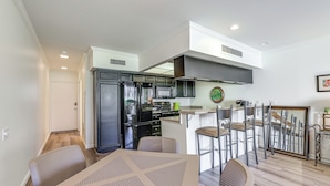 A modern kitchen with dark cabinets, a stainless steel refrigerator, and a microwave. There is a dining area with a table and chairs, and a bar area with stools. - Mtn-view Condo w/ Pool Access in Palm Springs! (Palm Springs)