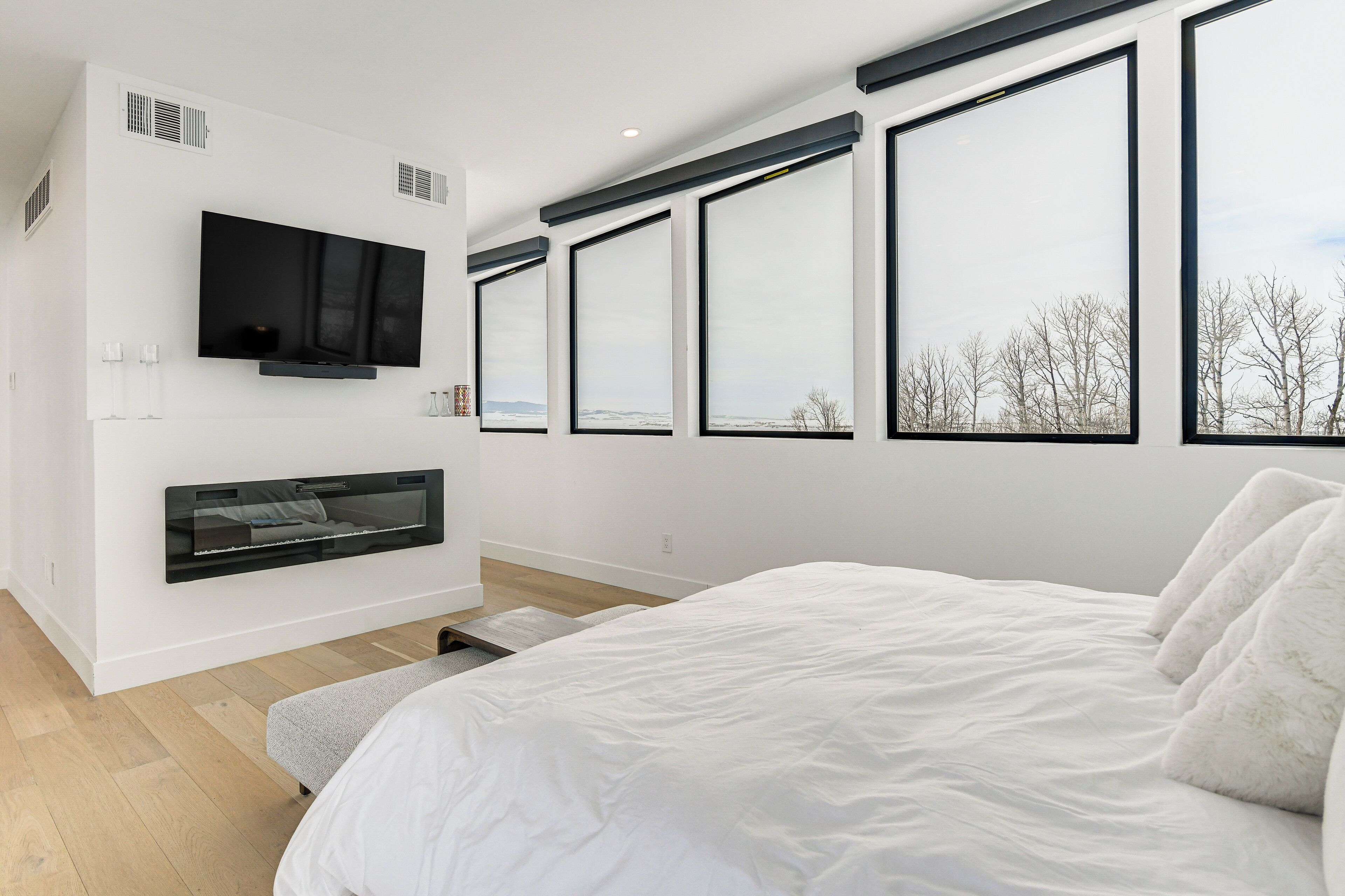 A modern bedroom with a large bed, a mounted TV, and a fireplace.