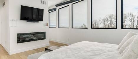 A modern bedroom with a large bed, a mounted TV, and a fireplace.