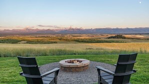 A circular fire pit with two Adirondack chairs facing it, set on a gravel area with a view of distant mountains and fields. - Hot Tub, 23 Mi to Grand Targhee: Luxe Retreat (Tetonia)