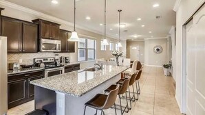 A modern kitchen with dark cabinets, a granite countertop, and a central island with bar stools. - Gorgeous 5Bd w Private Pool Windsor Westside 8893 (Kissimmee)