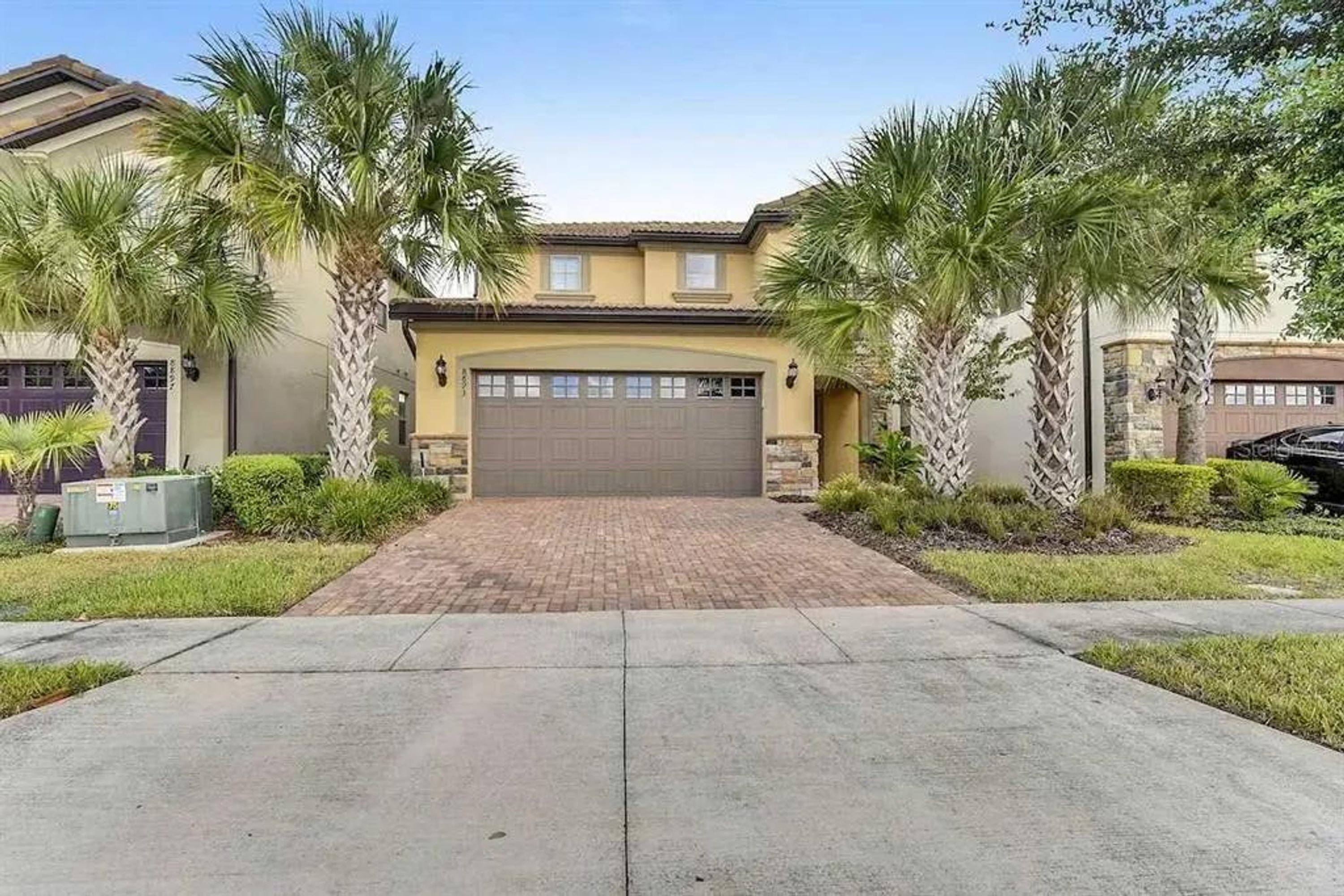 A residential house with a brick driveway, a garage, and palm trees.