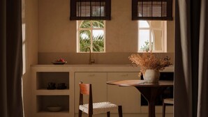 Een keuken met een ronde tafel, een stoel, een spoelbak en een raam met jaloezieën.
