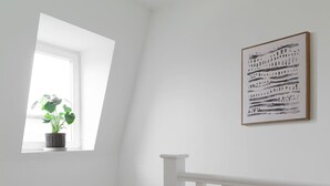 Un escalier avec des rampes blanches, une petite fenêtre ornée d’une plante et une œuvre d’art encadrée accrochée au mur.