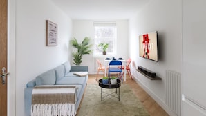 Un salon moderne avec un canapé, une table basse, un téléviseur fixé au mur et une fenêtre agrémentée d’une plante.